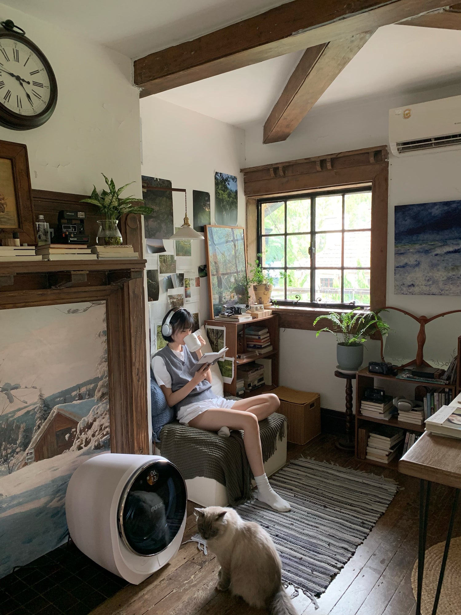 Person sitting in a cozy room with a cat, surrounded by books and decor. one morus c2 dryer set beside.